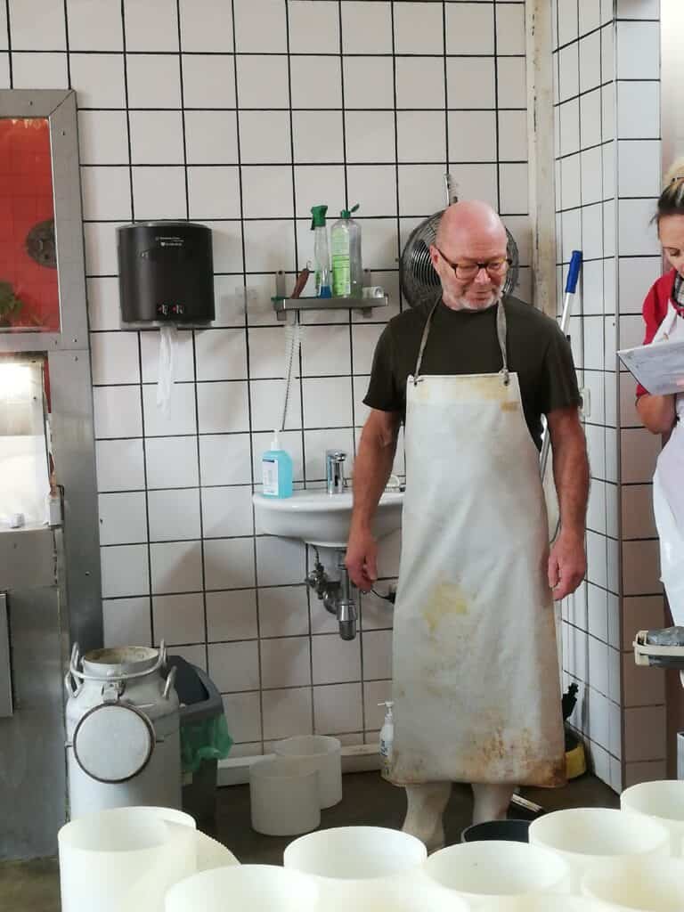 Meister Paget mit Schürze steht in einer gefliesten Käserei hinter weißen Käseformen