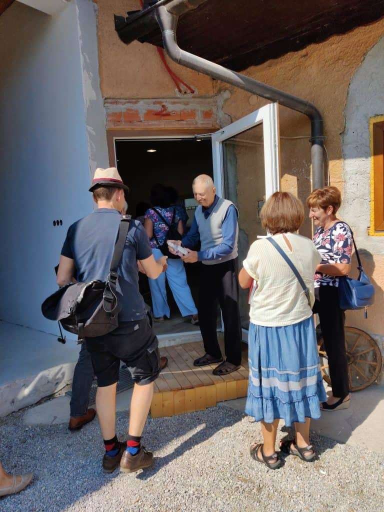 Ein älterer Mann begrüßt eine Besuchergruppe an der offenen Eingangstür eines Gebäudes in Slowenien